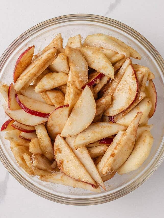 Nothing says fall like an old-fashioned pear pie! Juicy, tender pears in a flaky pastry then topped with a golden crumble are the perfect blend of sweet fruit and buttery crunch. Fresh pear slices tossed with sugar and cinnamon mixture in a clear glass bowl.