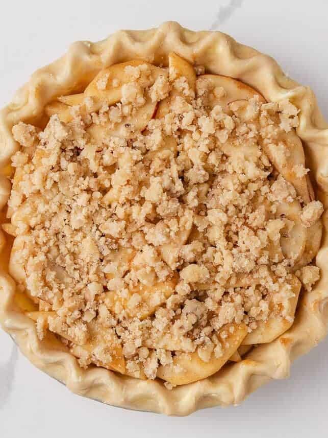 Nothing says fall like an old-fashioned pear pie! Juicy, tender pears in a flaky pastry then topped with a golden crumble are the perfect blend of sweet fruit and buttery crunch. Overhead view of pear pie in crust topped with streusel crumbs, ready for the oven.