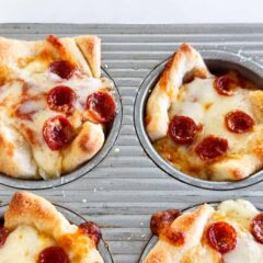 Freshly baked pepperoni pizza muffins cooling in a muffin tin, cheese melted and golden.