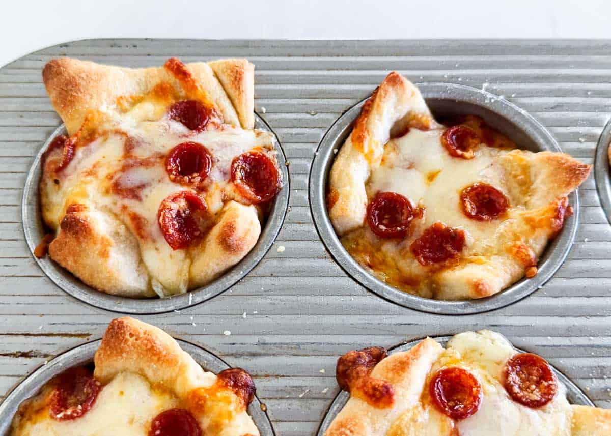 Freshly baked pepperoni pizza muffins cooling in a muffin tin, cheese melted and golden.