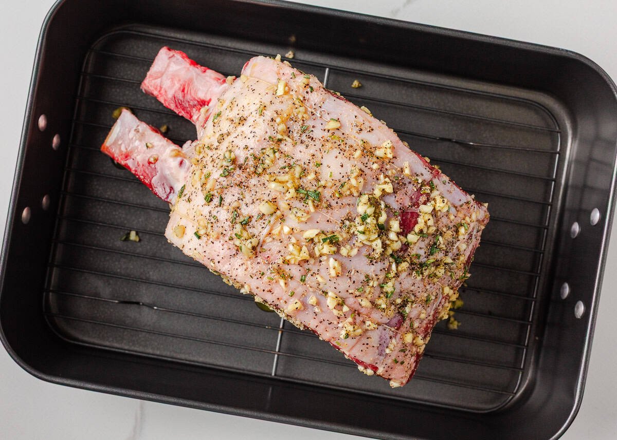 Juicy, flavorful, and perfectly cooked prime rib made right at home! With a beautifully seasoned crust and bone-in presentation, it's festive for the holidays or special occasions. Raw prime rib coated with a garlic and rosemary rub in a roasting pan.