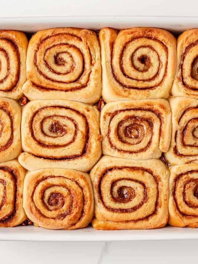 Warm, gooey, and dripping in a maple caramel glaze and pecan topping, these homemade sticky buns are the perfect bake for your next holiday brunch or cozy weekend morning! Freshly baked sticky buns in a white baking dish, golden brown with visible cinnamon swirls.
