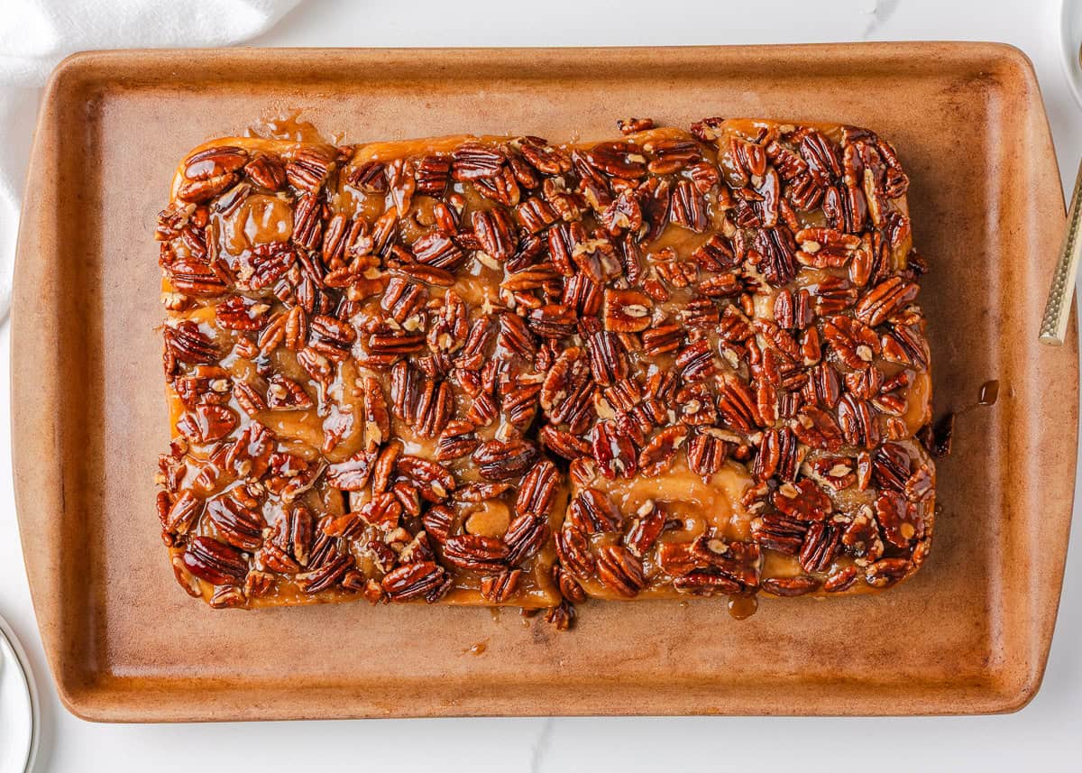 Warm, gooey, and dripping in a maple caramel glaze and pecan topping, these homemade sticky buns are the perfect bake for your next holiday brunch or cozy weekend morning! Sticky buns inverted onto a serving tray with glossy caramel pecan topping covering the surface.