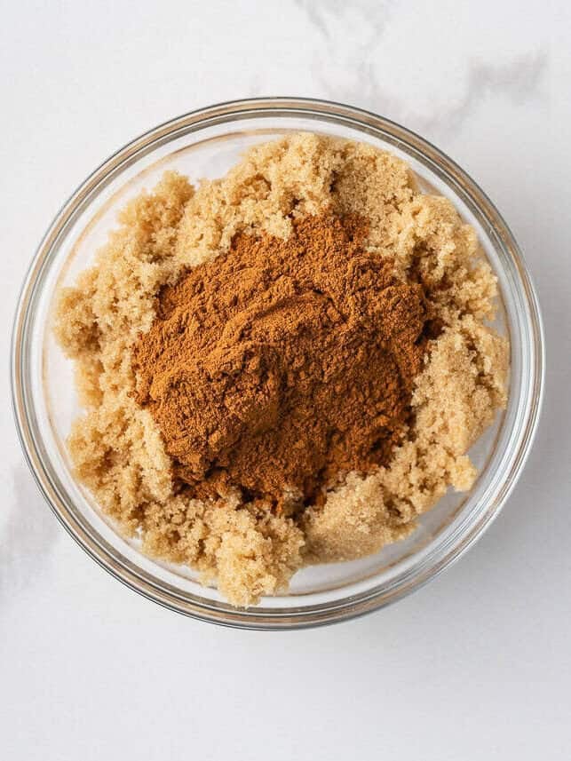 Warm, gooey, and dripping in a maple caramel glaze and pecan topping, these homemade sticky buns are the perfect bake for your next holiday brunch or cozy weekend morning! Small bowl filled with brown sugar and ground cinnamon for sticky bun filling.