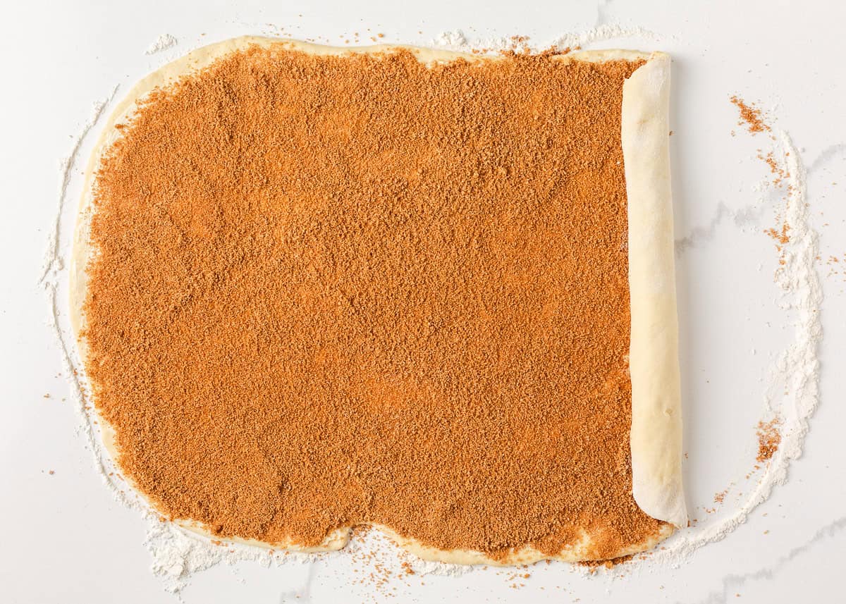 Warm, gooey, and dripping in a maple caramel glaze and pecan topping, these homemade sticky buns are the perfect bake for your next holiday brunch or cozy weekend morning! Sticky bun dough rolled out into a rectangle and sprinkled evenly with a brown sugar and cinnamon mixture.