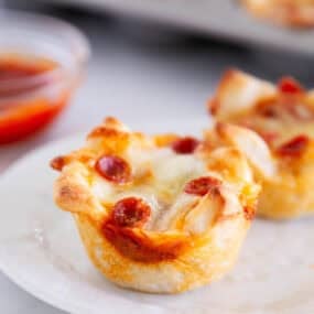 Golden, cheesy pizza muffin topped with mini pepperoni on a white plate, ready to eat.