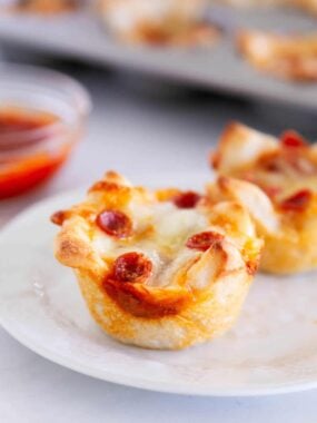 Golden, cheesy pizza muffin topped with mini pepperoni on a white plate, ready to eat.