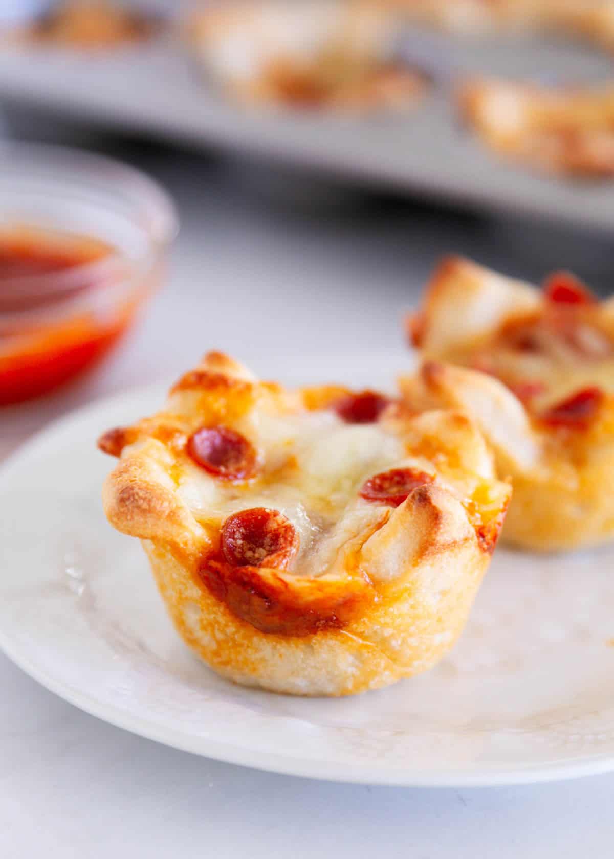 Pepperoni pizza muffin served on a white plate with pizza sauce for dipping in the background.