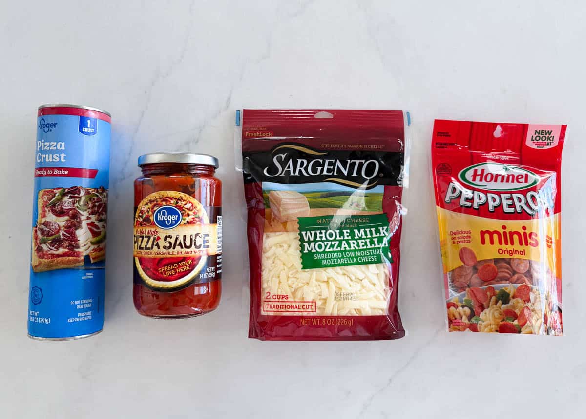 Store-bought refrigerated pizza dough, pizza sauce, shredded mozzarella, and mini pepperoni arranged on a countertop.