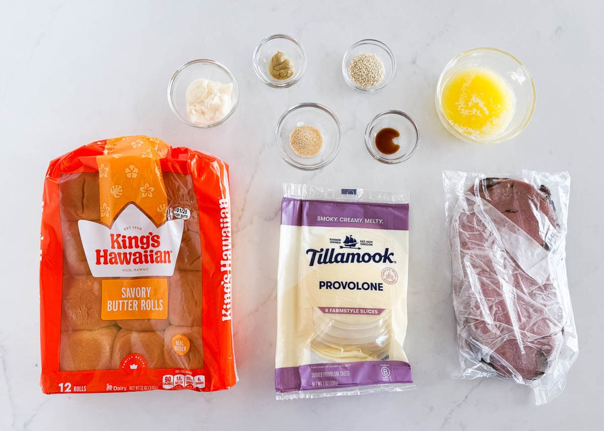 Roast beef slider ingredients including Hawaiian rolls, provolone slices, deli roast beef, melted butter, mayo, sesame seeds, garlic powder, Dijon and Worcestshire.