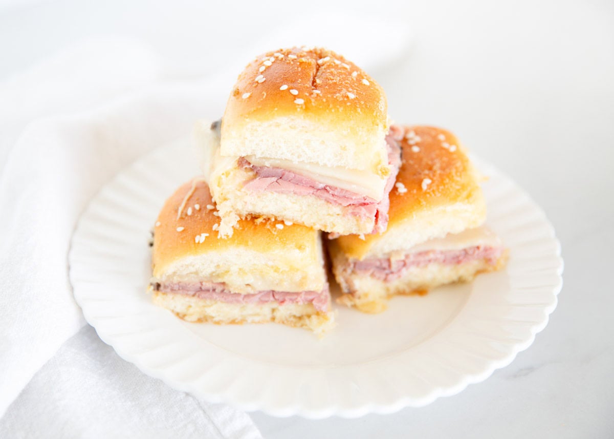 Three roast beef sliders stacked on a white plate ready to serve.