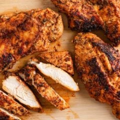 Blackened chicken breasts on a cutting board with tender slices arranged beside them