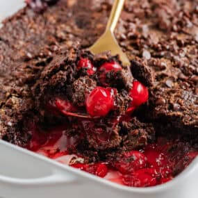 Warm chocolate cherry dump cake in a white baking dish, with juicy cherries and melty chocolate cake scooped up.