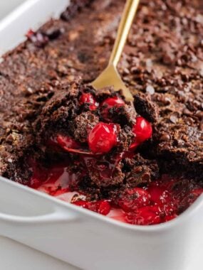 Warm chocolate cherry dump cake in a white baking dish, with juicy cherries and melty chocolate cake scooped up.