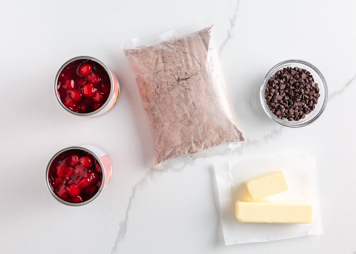 Rich, gooey, and packed with chocolate cherry flavor, this chocolate cherry dump cake is made with only 4 ingredients and minimal prep. It's a quick and easy indulgent dessert! Ingredients for chocolate cherry dump cake laid out on a counter: cherry pie filling, chocolate cake mix, mini chocolate chips, and butter.