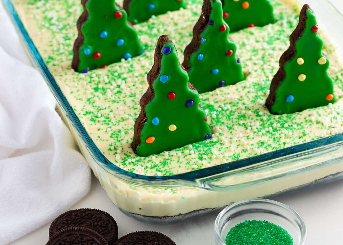 This Christmas dirt cake is a simple, no-bake dessert made with an Oreo crust, creamy whipped topping pudding layer and decorated with Little Debbie Christmas trees! Close-up of creamy Christmas dirt cake with Oreo cookie crust, green sprinkles, and Christmas tree brownies decorated with colorful candy pieces.