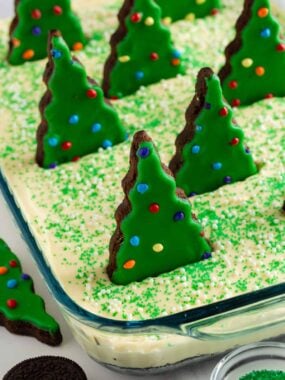 Christmas dirt cake in a glass 9x13 pan covered in green sprinkles and white nonpareils, topped with rows of standing Little Debbie Christmas tree brownies.