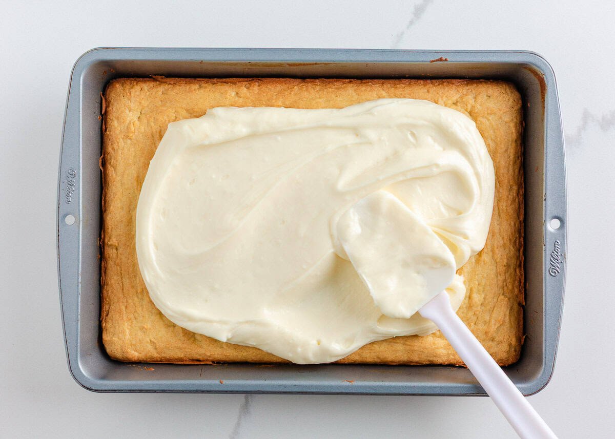 Spreading creamy cream cheese frosting over baked Christmas sugar cookie bars in a 9x13 pan.