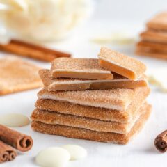 Churro toffee squares stacked neatly with a bowl of white chocolate melting wafers behind them.