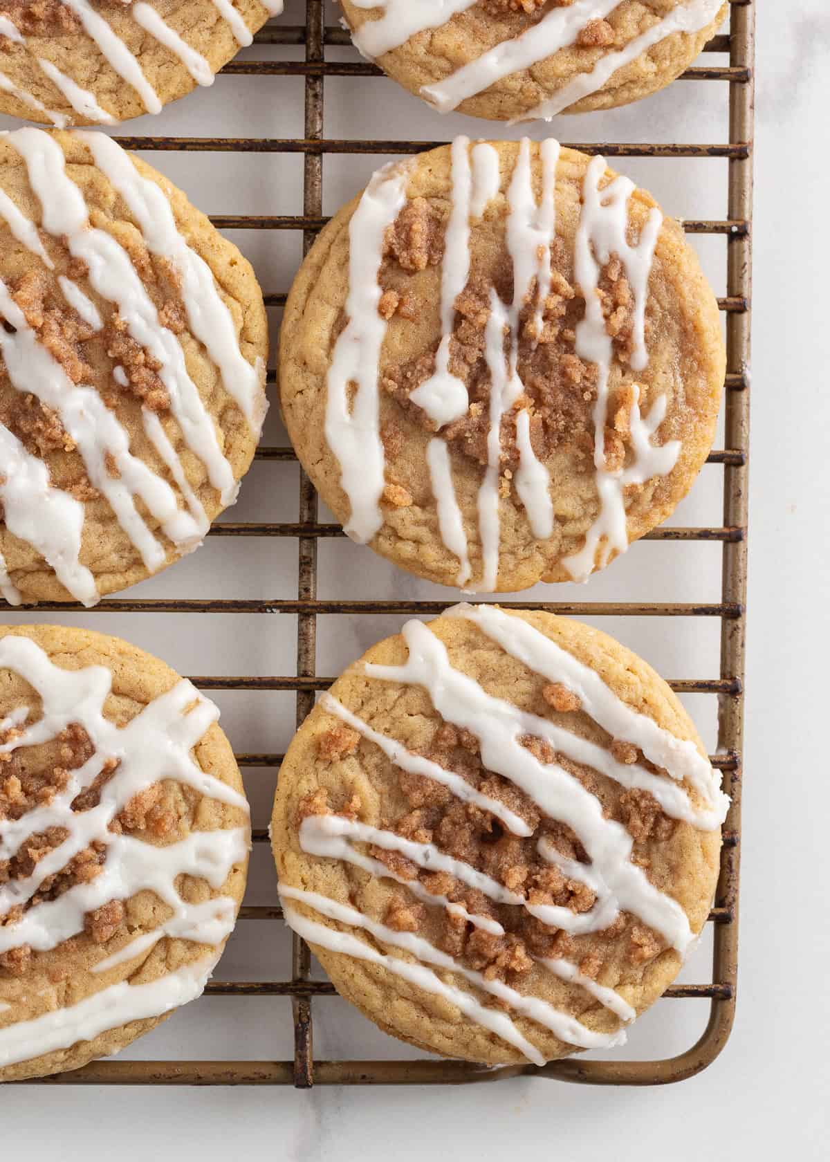 Originally inspired by The Gilmore Girls, these coffee cake cookies are made with a soft and chewy cinnamon-infused brown sugar cookie with a crumb topping and vanilla glaze! Freshly baked coffee cake cookies cooling on a wire rack with powdered sugar glaze.