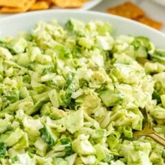 Close-up of chopped green goddess salad made with cabbage, cucumbers, avocado, and green onions in a white bowl.