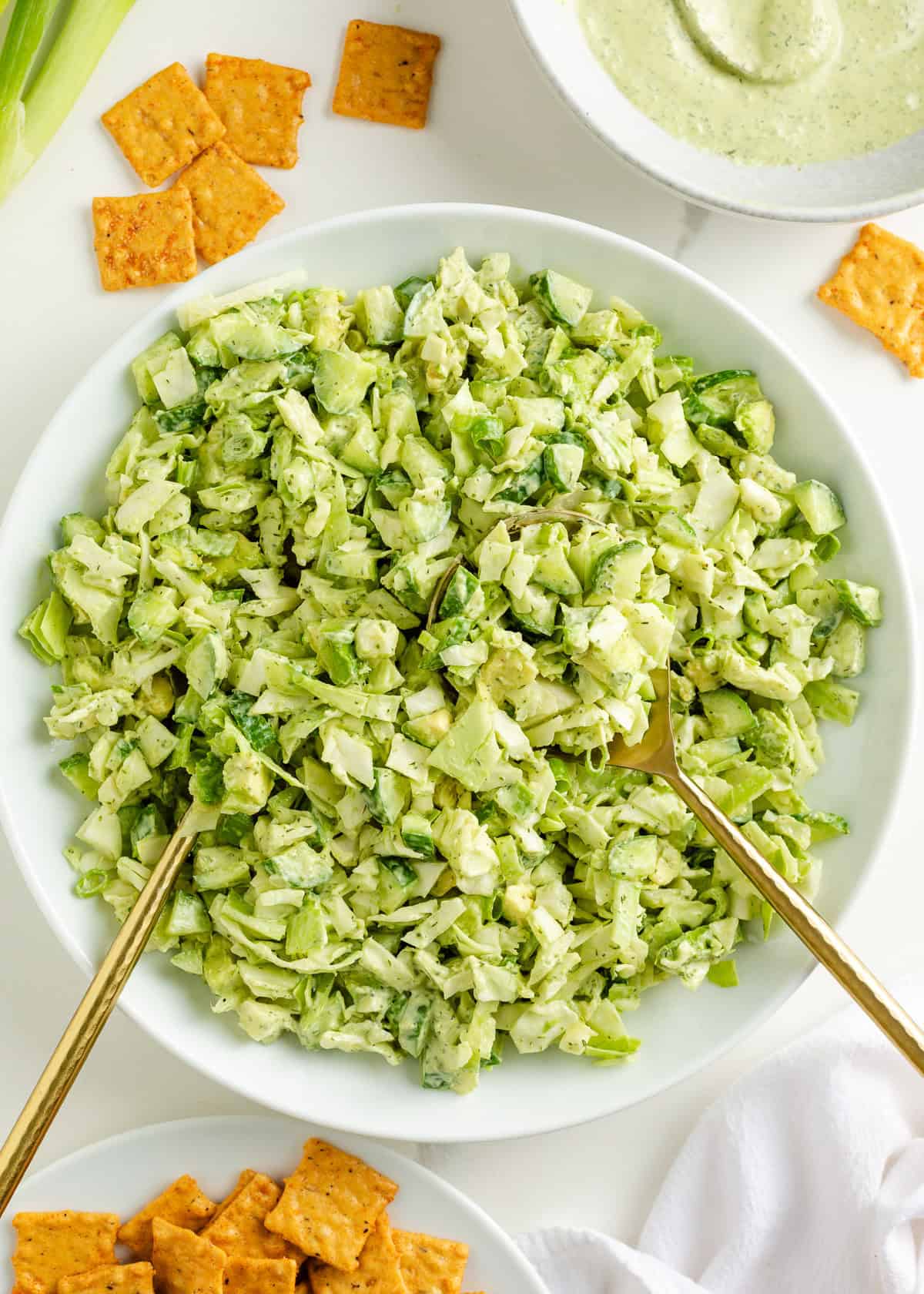 Large serving bowl filled with green goddess salad and gold salad tongs.