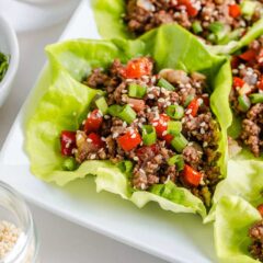 Asian beef lettuce wraps on a white platter with a bowl of sliced green onions on the side.