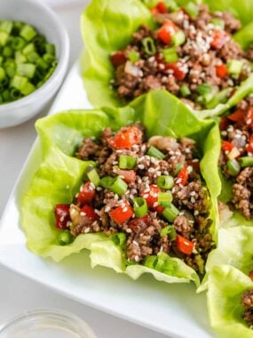 Close-up of Asian-style ground beef lettuce wraps topped with chopped green onions and sesame seeds.