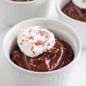 Creamy homemade chocolate pudding in a ramekin topped with a dollop of whipped cream and chocolate shavings.
