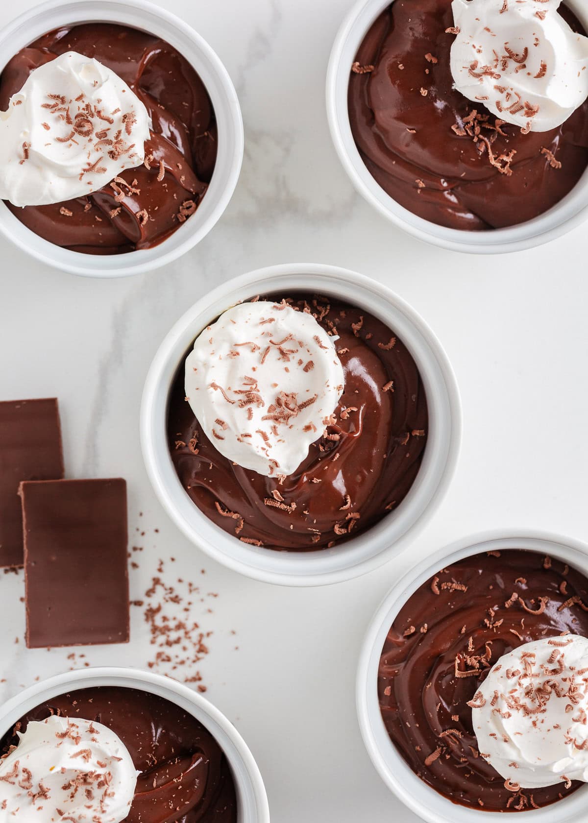 This homemade chocolate pudding is rich, creamy, and easy to make from scratch with just a few simple ingredients. It's just the treat when a chocolate craving hits! Homemade chocolate pudding cups arranged on a counter, each topped with fresh whipped cream.