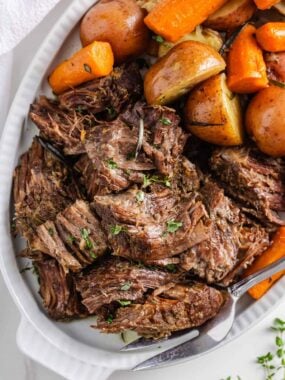 Juicy Instant Pot pot roast served with halved red potatoes and carrots on a white platter, showing how soft and shredded the beef becomes after pressure cooking.