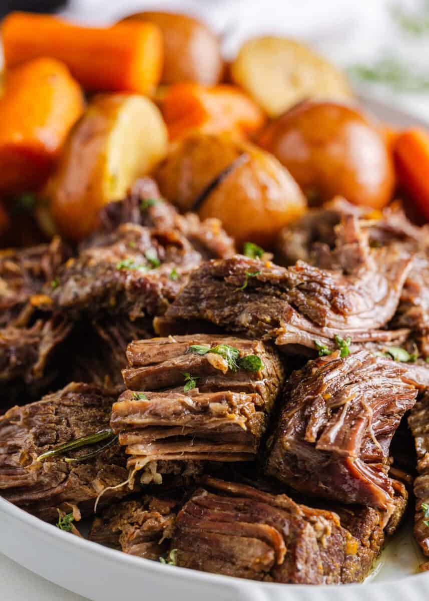 Close-up of Instant Pot pot roast showing tender shredded beef pieces with carrots and potatoes in the background, garnished with fresh herbs.