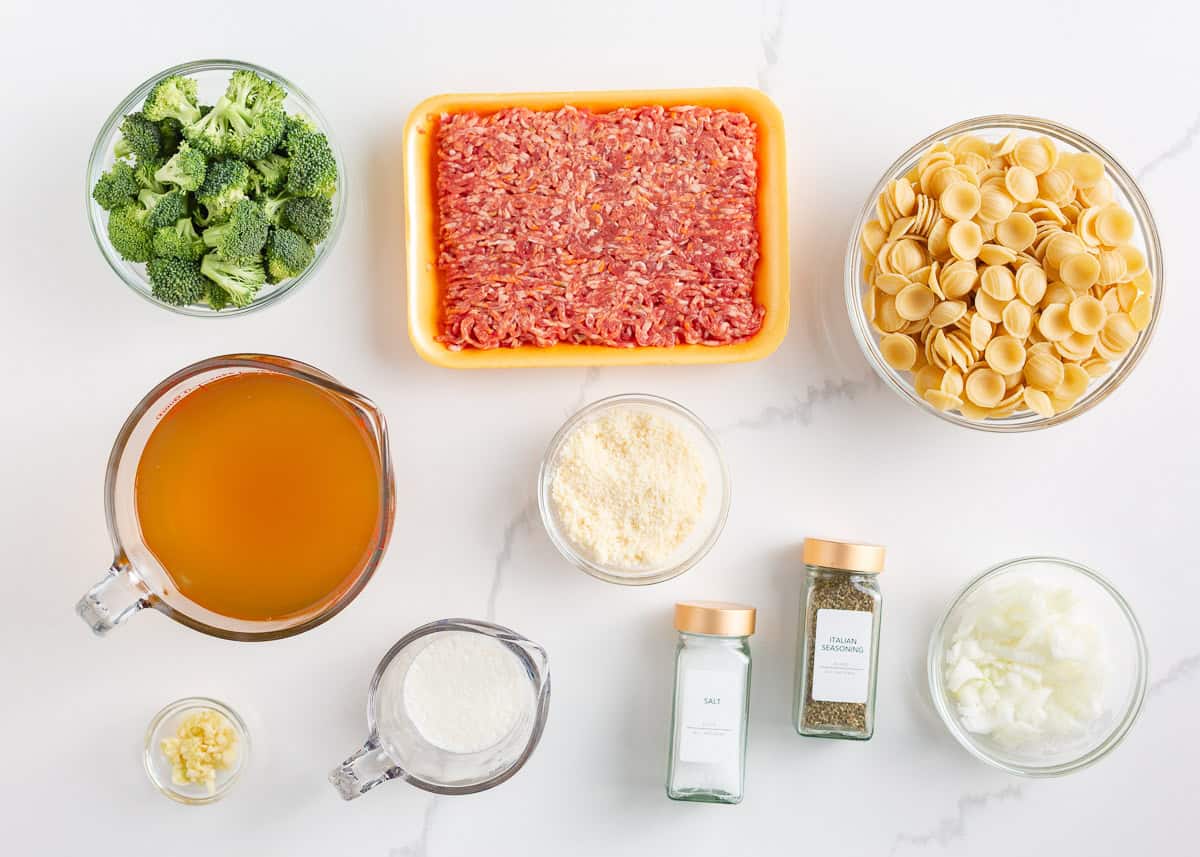 This orecchiette pasta with sausage and broccoli is simmered in a light, creamy sauce until the pasta is tender and the broccoli is bright. It’s a comforting one-pan meal ready in 30 minutes! Bowls of broccoli, ground sausage, dry orecchiette pasta, broth, grated Parmesan, cream, garlic, onion, salt, and Italian seasoning arranged on a white countertop.