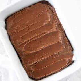 Overhead shot of brownies fully frosted with chocolate brownie frosting in a white baking dish.