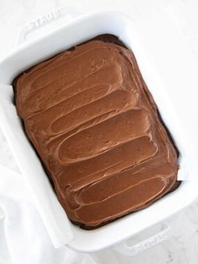 Overhead shot of brownies fully frosted with chocolate brownie frosting in a white baking dish.