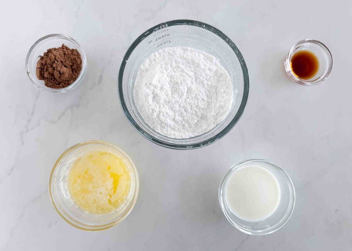 This thick and creamy brownie frosting sets up perfectly and brings a nostalgic, rich chocolate flavor to homemade or boxed brownies. Overhead view of ingredients for brownie frosting, including cocoa powder, powdered sugar, melted butter, milk, and vanilla