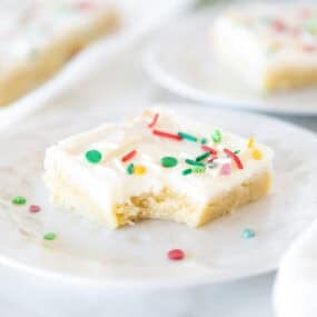 Soft and chewy Christmas sugar cookie bar with cream cheese frosting and sprinkles, with a bite taken out.