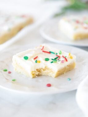 Soft and chewy Christmas sugar cookie bar with cream cheese frosting and sprinkles, with a bite taken out.