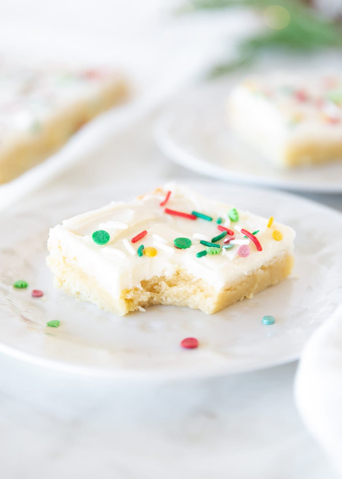 Soft and chewy Christmas sugar cookie bar with cream cheese frosting and sprinkles, with a bite taken out.