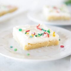 Soft and chewy Christmas sugar cookie bar with cream cheese frosting and sprinkles on a plate.