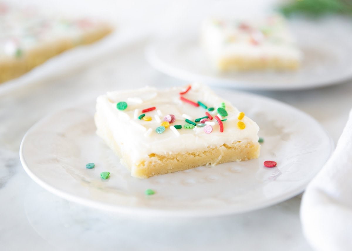 Frosted Christmas sugar cookie bar topped with colorful sprinkles on a white plate.