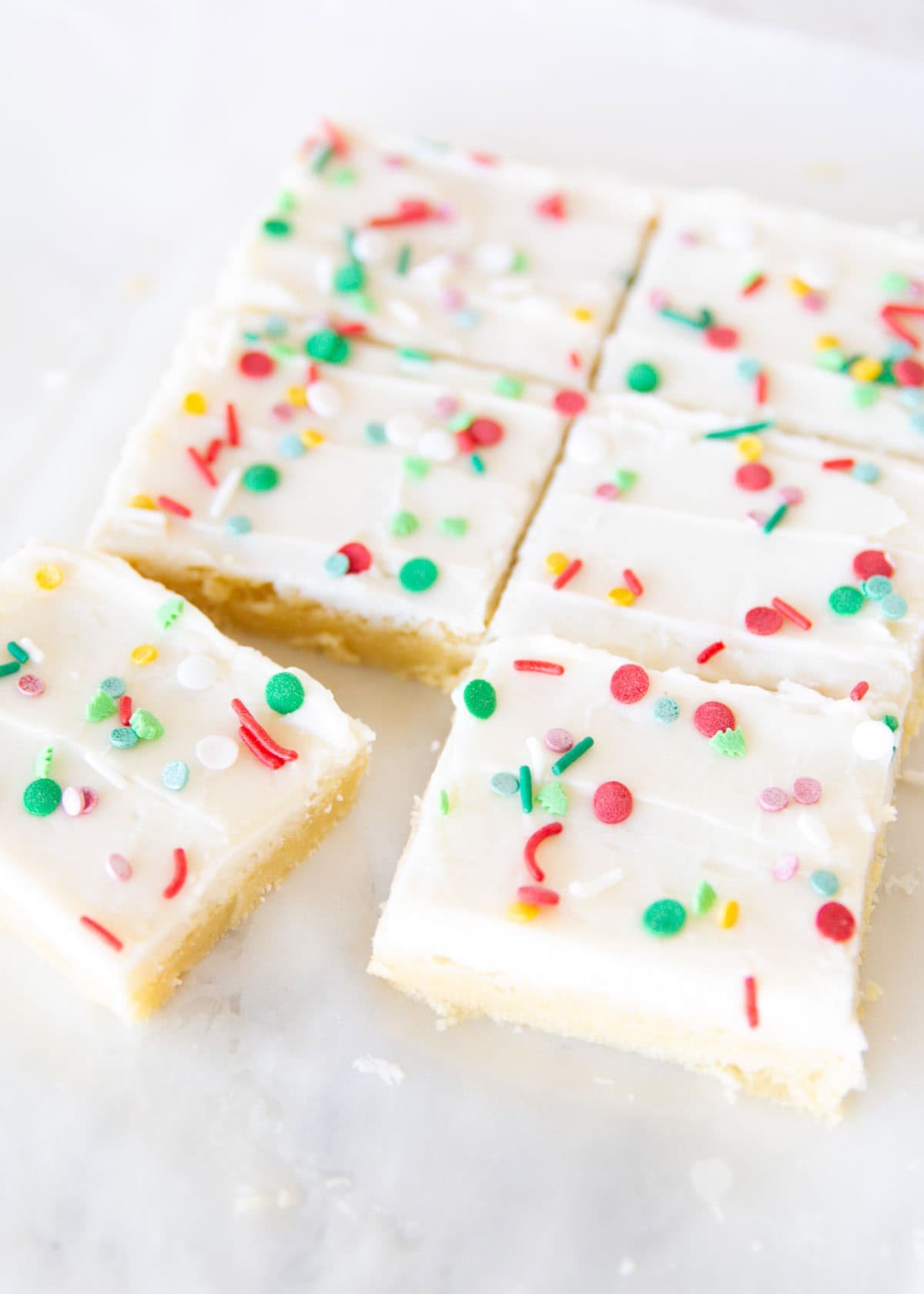 Soft Christmas sugar cookie bars frosted with cream cheese icing and topped with Christmas sprinkles, cut into squares.
