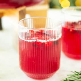 Close-up of a glass filled with sparkling cranberry punch and floating cranberries, set on a marble surface.