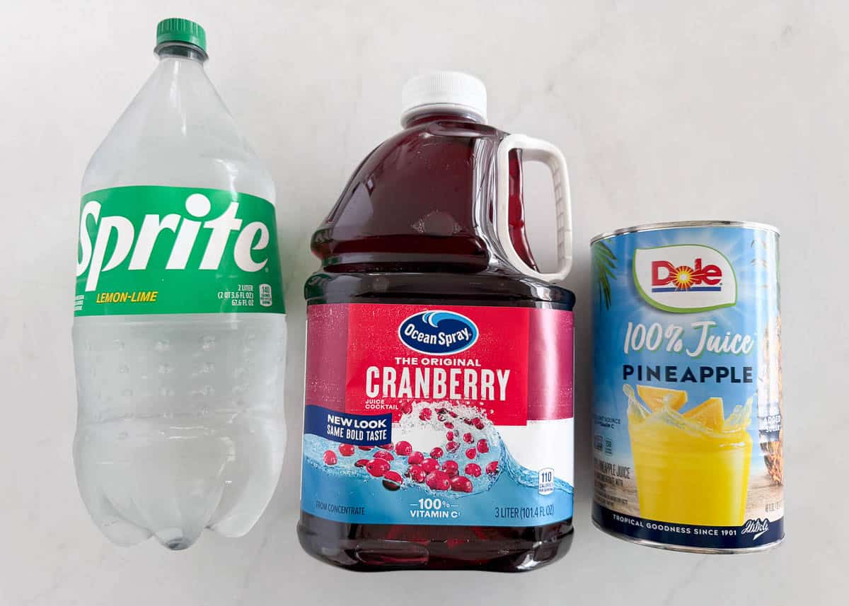 This easy cranberry punch is fizzy, festive, and perfect for holiday gatherings. Just mix juices, add fruit on top, and you’ve got a crowd-pleasing Christmas drink everyone loves. Ingredients for cranberry punch displayed on a counter including Sprite, cranberry juice, and a can of pineapple juice.