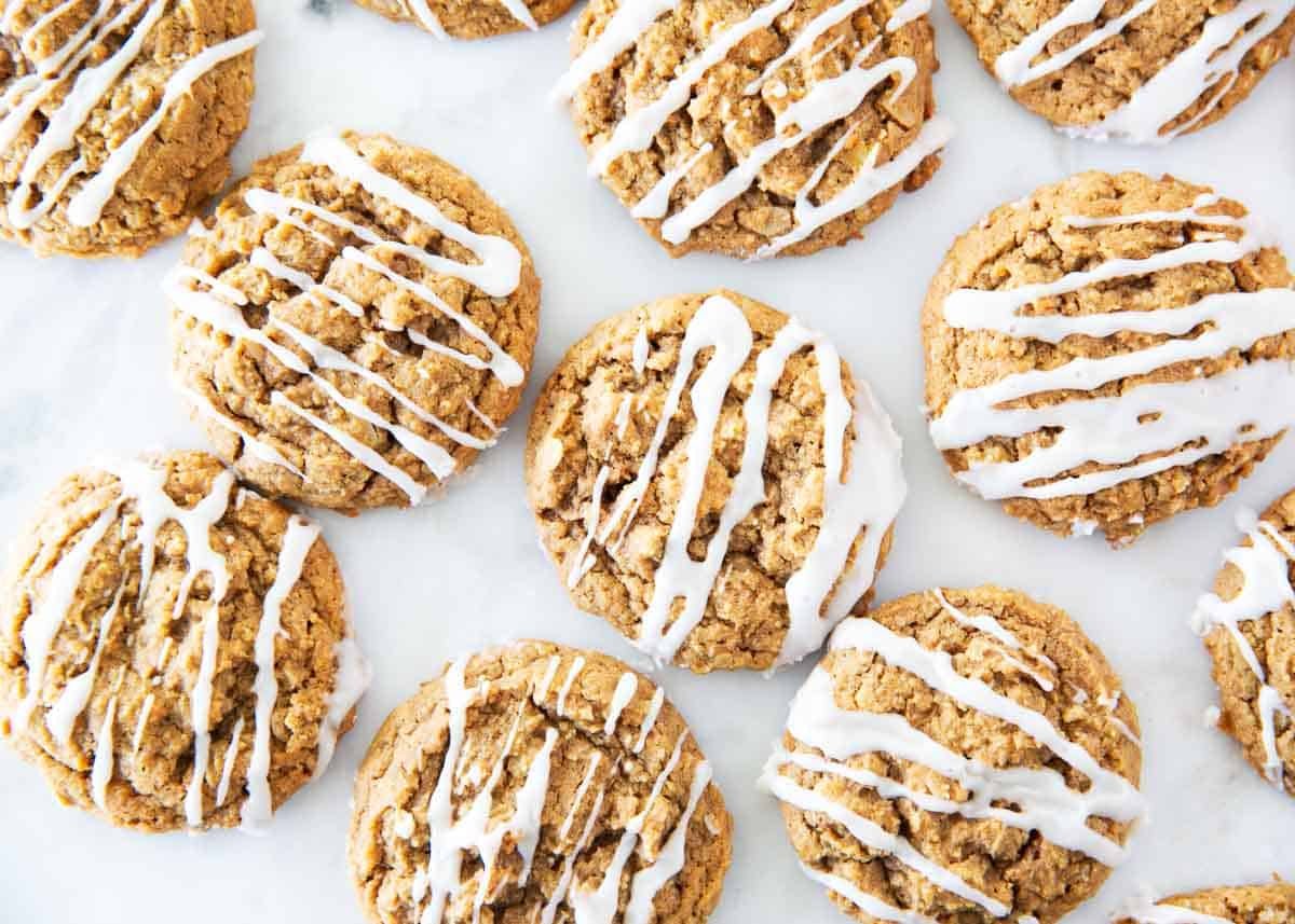 Freshly baked gingerbread oatmeal cookies with white icing drizzle arranged on a marble countertop.