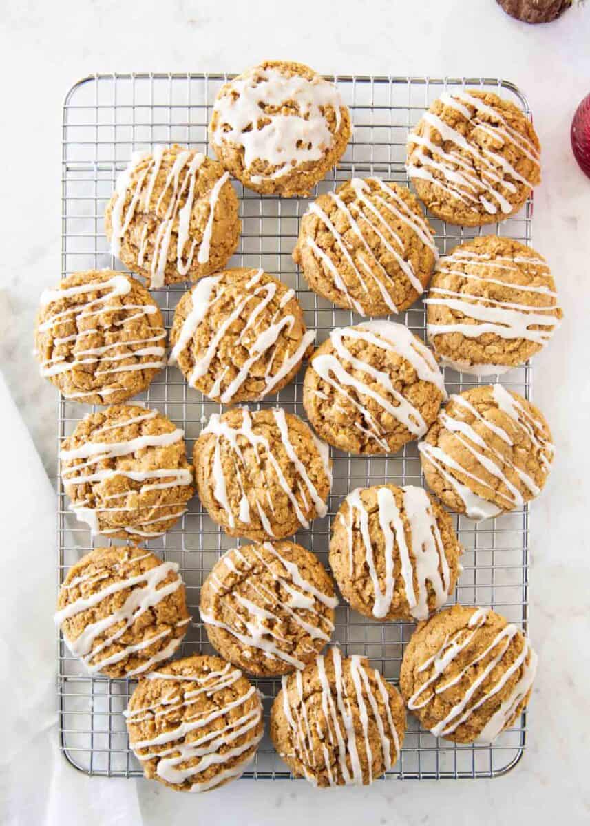 Gingerbread oatmeal cookies cooling on a wire rack with vanilla glaze drizzled on top.