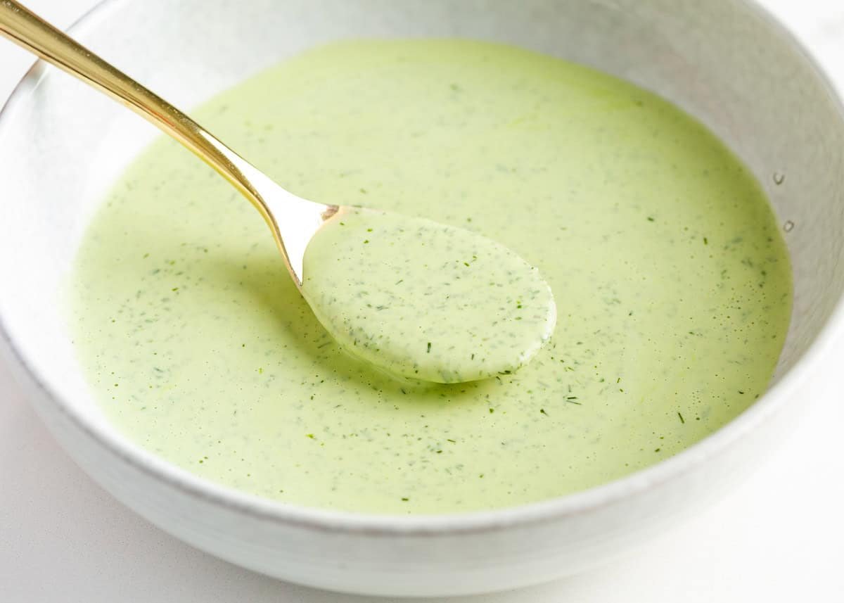 Learn to make this TikTok Green Goddess Salad with the best, most flavorful homemade green goddess salad dressing you're going to want to put on everything! Green goddess dressing in a white bowl, with a spoon lifting a scoop of creamy herb sauce.