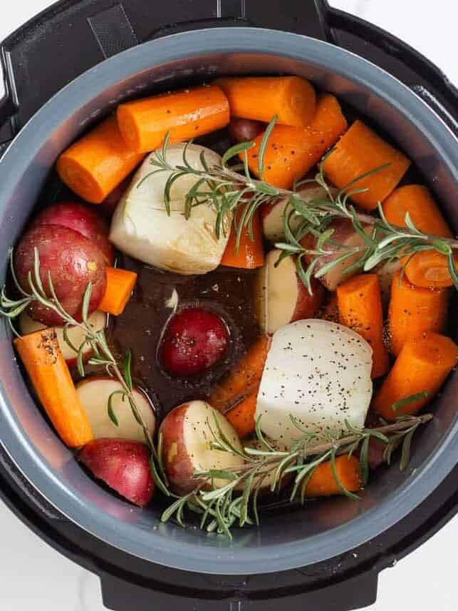 Carrots, red potatoes, onion, fresh rosemary, and broth layered around the seared roast in the Instant Pot before cooking.