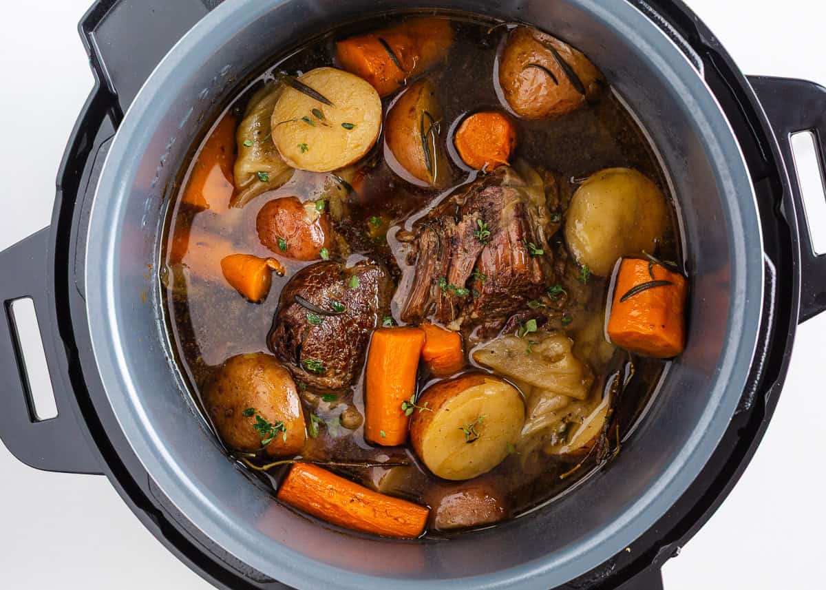 Instant Pot pot roast simmering in beef broth with baby potatoes, carrots, and onions after pressure cooking.