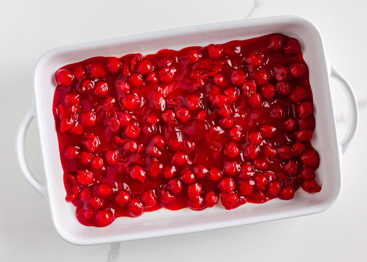Rich, gooey, and packed with chocolate cherry flavor, this chocolate cherry dump cake is made with only 4 ingredients and minimal prep. It's a quick and easy indulgent dessert! Cherry pie filling spread evenly in a white baking dish for the base of chocolate cherry dump cake.